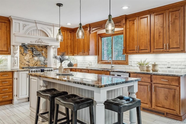kitchen with a sink, a breakfast bar area, brown cabinets, tasteful backsplash, and dark stone countertops
