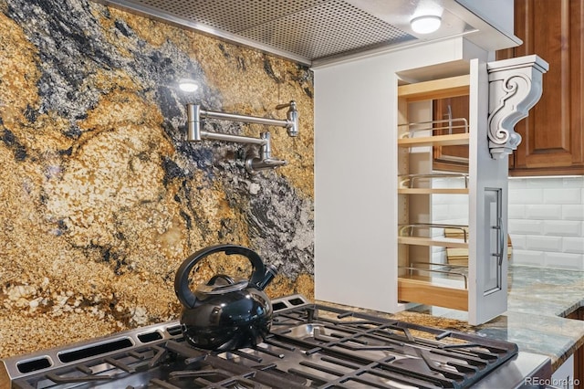 kitchen view of pot filler, backsplash, brown cabinets, and stone countertops