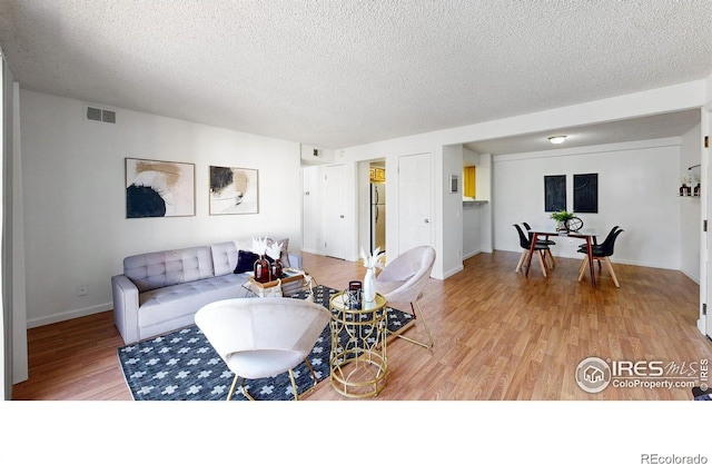 living room featuring a textured ceiling, light wood finished floors, visible vents, and baseboards