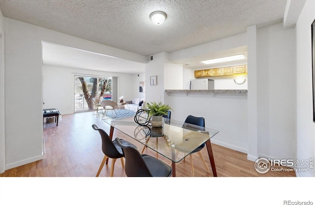 dining room with a textured ceiling, visible vents, light wood-style flooring, and baseboards