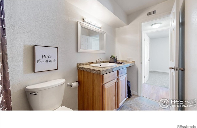 bathroom with toilet, vanity, visible vents, and baseboards