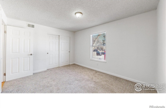 unfurnished bedroom featuring a textured ceiling, carpet flooring, visible vents, baseboards, and a closet