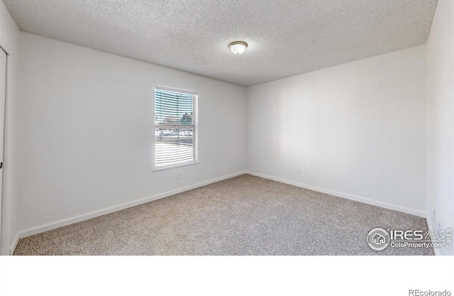 carpeted empty room featuring a textured ceiling and baseboards