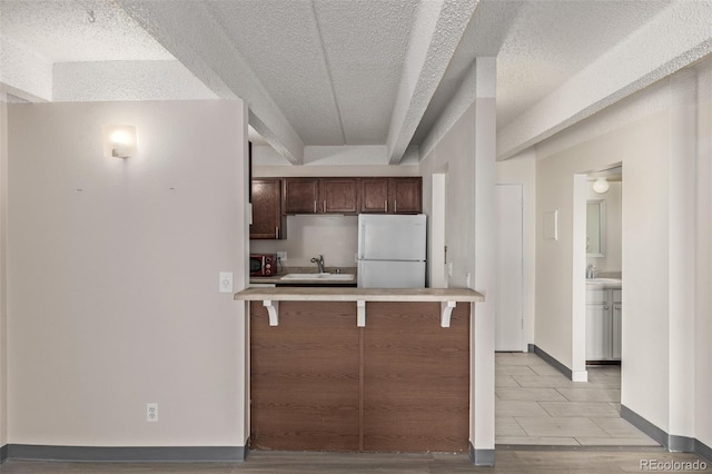 kitchen featuring a kitchen bar, sink, a textured ceiling, and white refrigerator