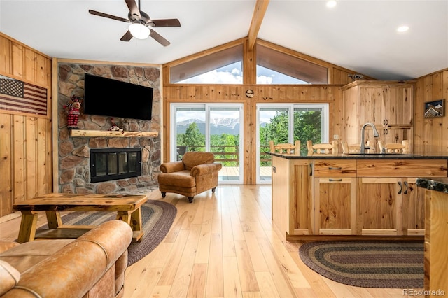 living room featuring wood walls, lofted ceiling, a stone fireplace, light hardwood / wood-style flooring, and ceiling fan