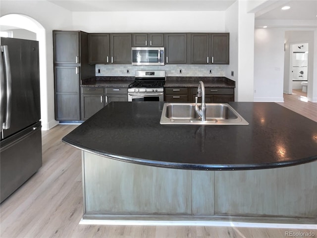 4735 S Cathay Ct, Aurora, CO 80015 - kitchen with appliances with stainless steel finishes, dark countertops, backsplash, a center island with sink, and light wood finished floors
