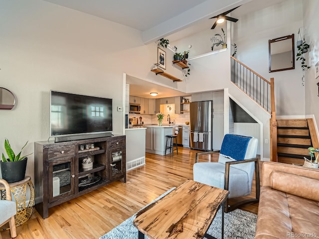 living area with a towering ceiling, stairway, light wood-style flooring, and a ceiling fan