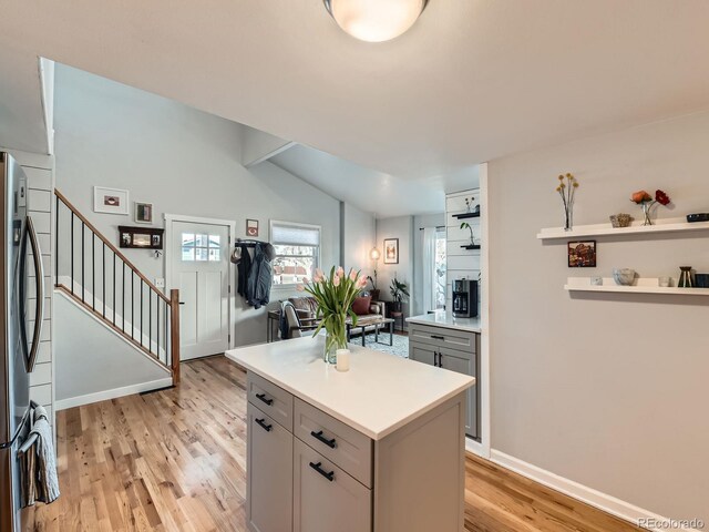 kitchen with light wood-style flooring, freestanding refrigerator, gray cabinetry, light countertops, and vaulted ceiling