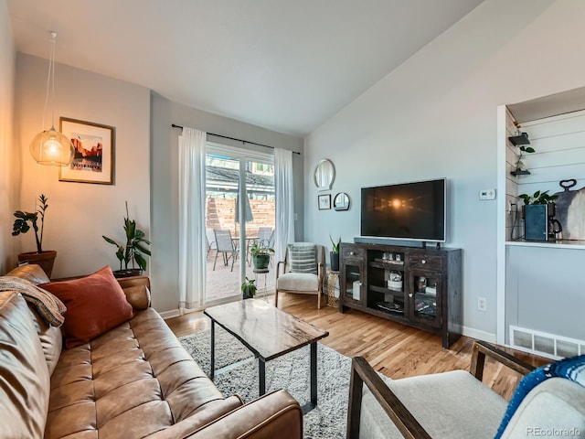 living area with lofted ceiling, wood finished floors, visible vents, and baseboards