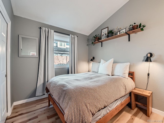 bedroom featuring light wood-type flooring, baseboards, and vaulted ceiling