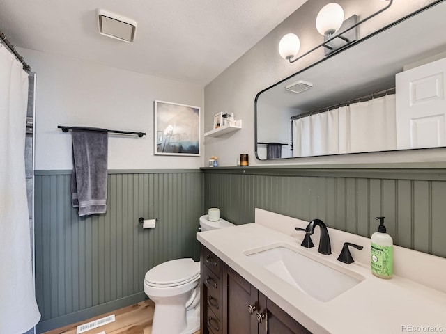 bathroom with visible vents, a wainscoted wall, toilet, wood finished floors, and vanity