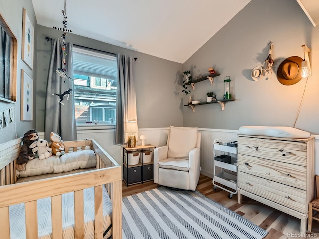 bedroom with vaulted ceiling, wood finished floors, and wainscoting