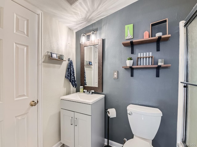 bathroom featuring vanity, toilet, a textured wall, and baseboards