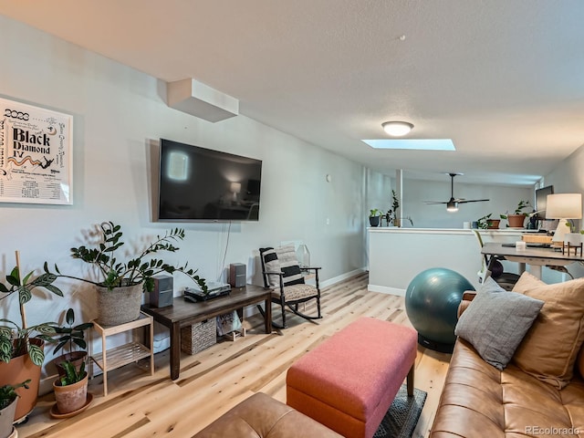 living area with a textured ceiling, wood finished floors, a skylight, baseboards, and ceiling fan