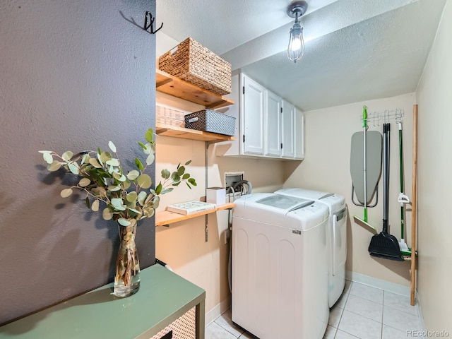 laundry room featuring a textured ceiling, washing machine and dryer, cabinet space, light tile patterned flooring, and baseboards