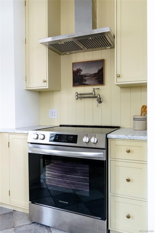 kitchen with light stone countertops, exhaust hood, electric range, and cream cabinets