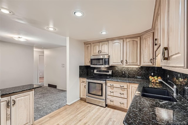 kitchen featuring stainless steel appliances, light brown cabinetry, a sink, and decorative backsplash