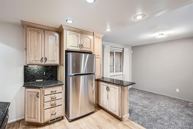 kitchen with decorative backsplash, dark stone countertops, freestanding refrigerator, a peninsula, and light brown cabinetry