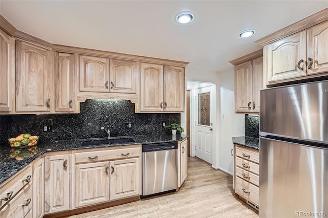 kitchen featuring stainless steel appliances, tasteful backsplash, light brown cabinets, a sink, and dark stone countertops