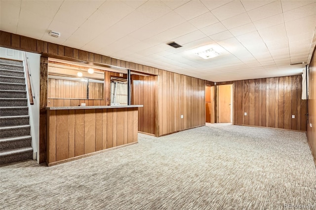 interior space with light carpet, wood walls, a bar, and stairs