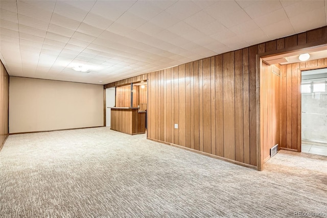 empty room featuring carpet floors, visible vents, and wooden walls