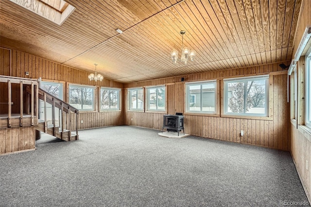 unfurnished sunroom featuring a chandelier, vaulted ceiling with skylight, a wood stove, and wood ceiling