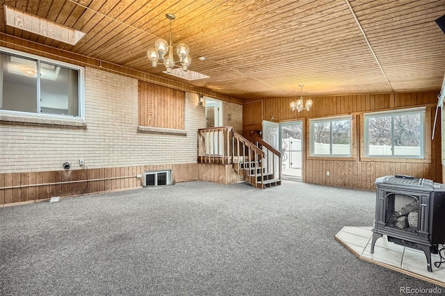 unfurnished living room with a wood stove, wooden walls, and an inviting chandelier