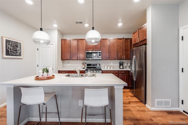 kitchen with pendant lighting, stainless steel appliances, a kitchen breakfast bar, and a center island with sink