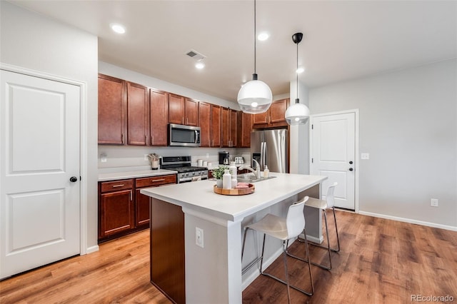 kitchen featuring light hardwood / wood-style flooring, a breakfast bar, appliances with stainless steel finishes, an island with sink, and decorative light fixtures