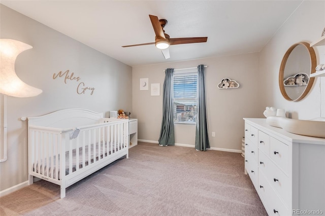 bedroom featuring light colored carpet, a nursery area, and ceiling fan