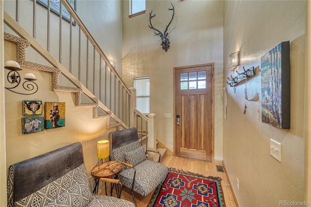 entrance foyer with stairway, light wood-style flooring, visible vents, and a towering ceiling