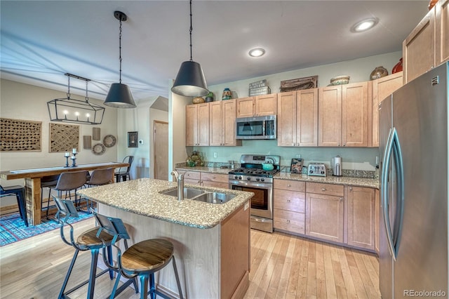 kitchen featuring light stone countertops, light wood-style flooring, a sink, appliances with stainless steel finishes, and a kitchen breakfast bar