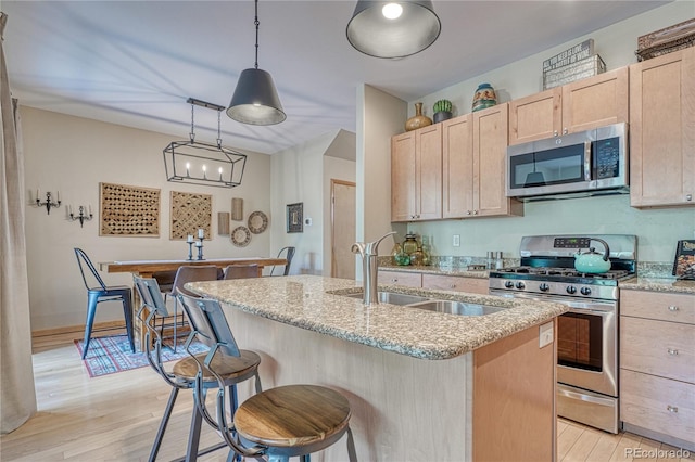 kitchen with light wood-style flooring, light brown cabinetry, a center island with sink, a sink, and stainless steel appliances