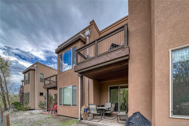 back of house with stucco siding, a patio, and a balcony