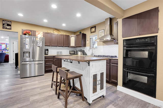 kitchen with stainless steel appliances, light wood-style floors, wood counters, dark brown cabinets, and wall chimney exhaust hood