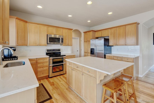 1864 Malibu Ct, Fort Lupton, CO 80621 - kitchen with stainless steel appliances, a sink, light brown cabinets, arched walkways, and a kitchen island