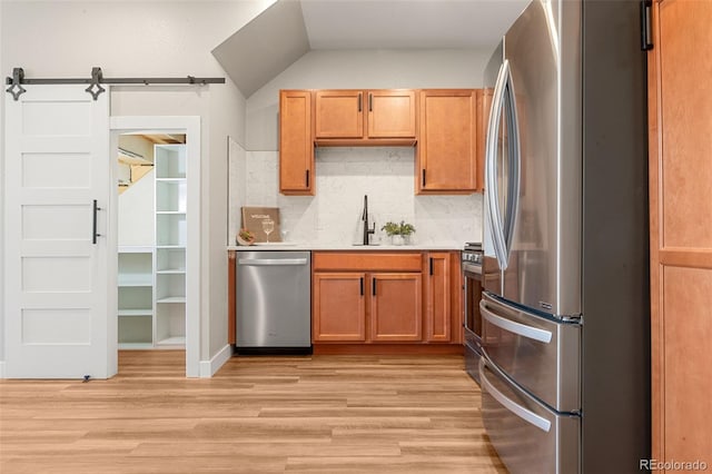 kitchen with a sink, stainless steel appliances, a barn door, and light wood-style flooring