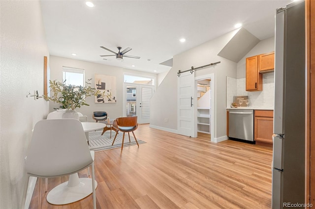 interior space featuring baseboards, ceiling fan, light wood-type flooring, a barn door, and stainless steel appliances