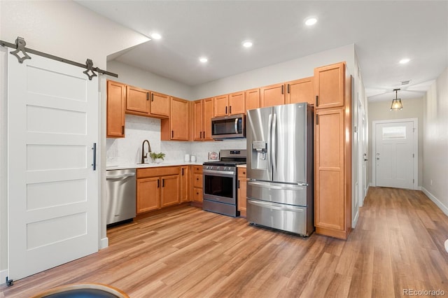 kitchen featuring a sink, light countertops, appliances with stainless steel finishes, a barn door, and light wood-type flooring