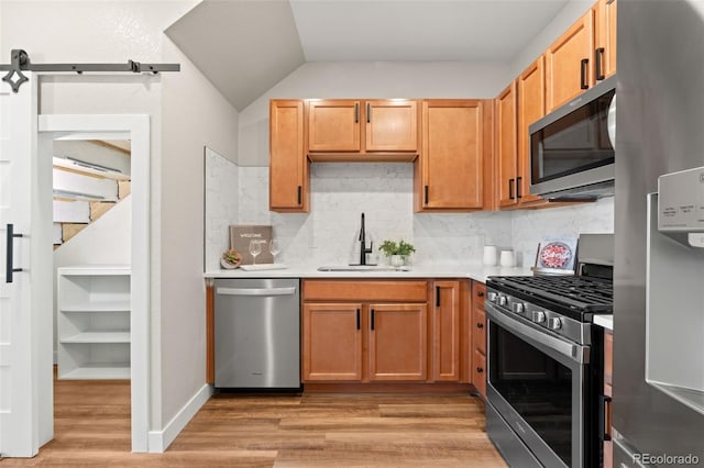 kitchen with light wood finished floors, a sink, stainless steel appliances, light countertops, and a barn door