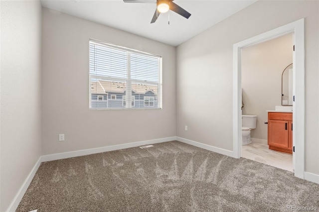 unfurnished bedroom with ceiling fan, baseboards, light carpet, and ensuite bath