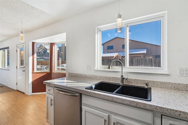 kitchen featuring dishwasher, sink, pendant lighting, a textured ceiling, and light wood-type flooring