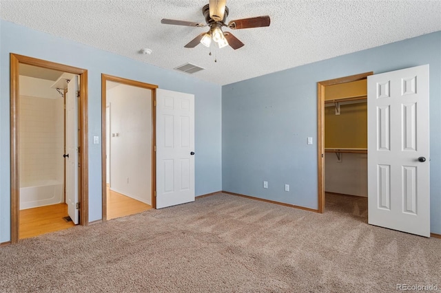 unfurnished bedroom featuring a walk in closet, light colored carpet, ensuite bath, and ceiling fan