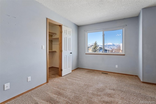 unfurnished bedroom featuring a spacious closet, light carpet, and a textured ceiling