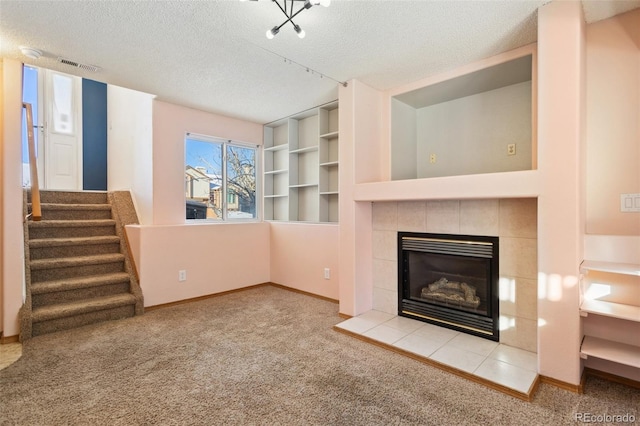 unfurnished living room featuring built in features, a textured ceiling, light carpet, and a tiled fireplace