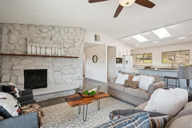 8045 S Wagon Wheel Rd, Morrison, CO 80465 - living area featuring wood finished floors, lofted ceiling, a skylight, a ceiling fan, and a stone fireplace