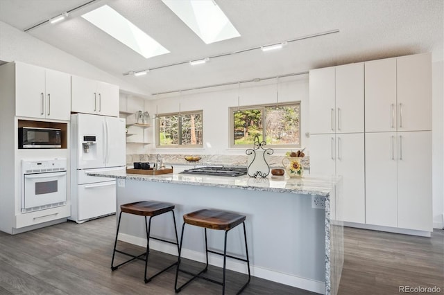 8045 S Wagon Wheel Rd, Morrison, CO 80465 - kitchen with white appliances, rail lighting, a skylight, a kitchen breakfast bar, and a textured ceiling