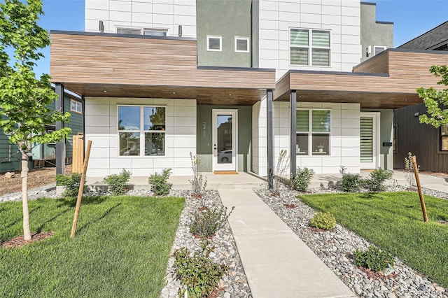doorway to property with covered porch, a lawn, and stucco siding