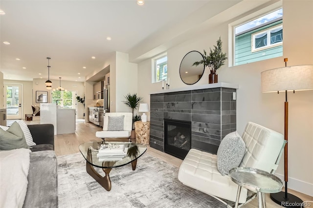 living room featuring light wood-style floors, recessed lighting, a glass covered fireplace, and baseboards