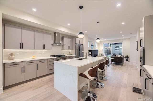 2466 S Cherokee St, Denver, CO 80223 - kitchen with wall chimney exhaust hood, gray cabinets, light wood-type flooring, appliances with stainless steel finishes, and recessed lighting